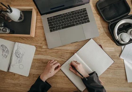 Persona aprendiendo, escribiendo en un bloc de notas y enfrente un computador con la guía cómo dibujar bodegón