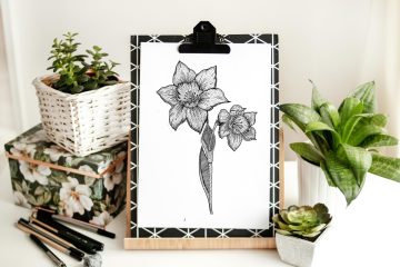 Dibujo de flores a lápiz colocado sobre una tabla de dibujo rodeada de plantas y materiales de arte.